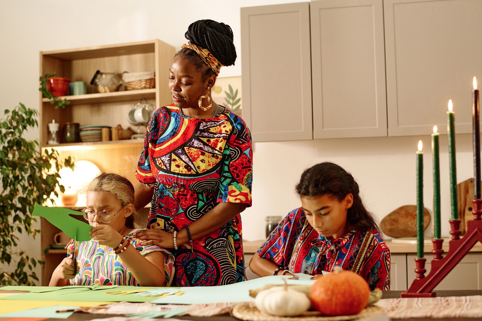 Young woman in national attire standing by her daughter cutting green paper