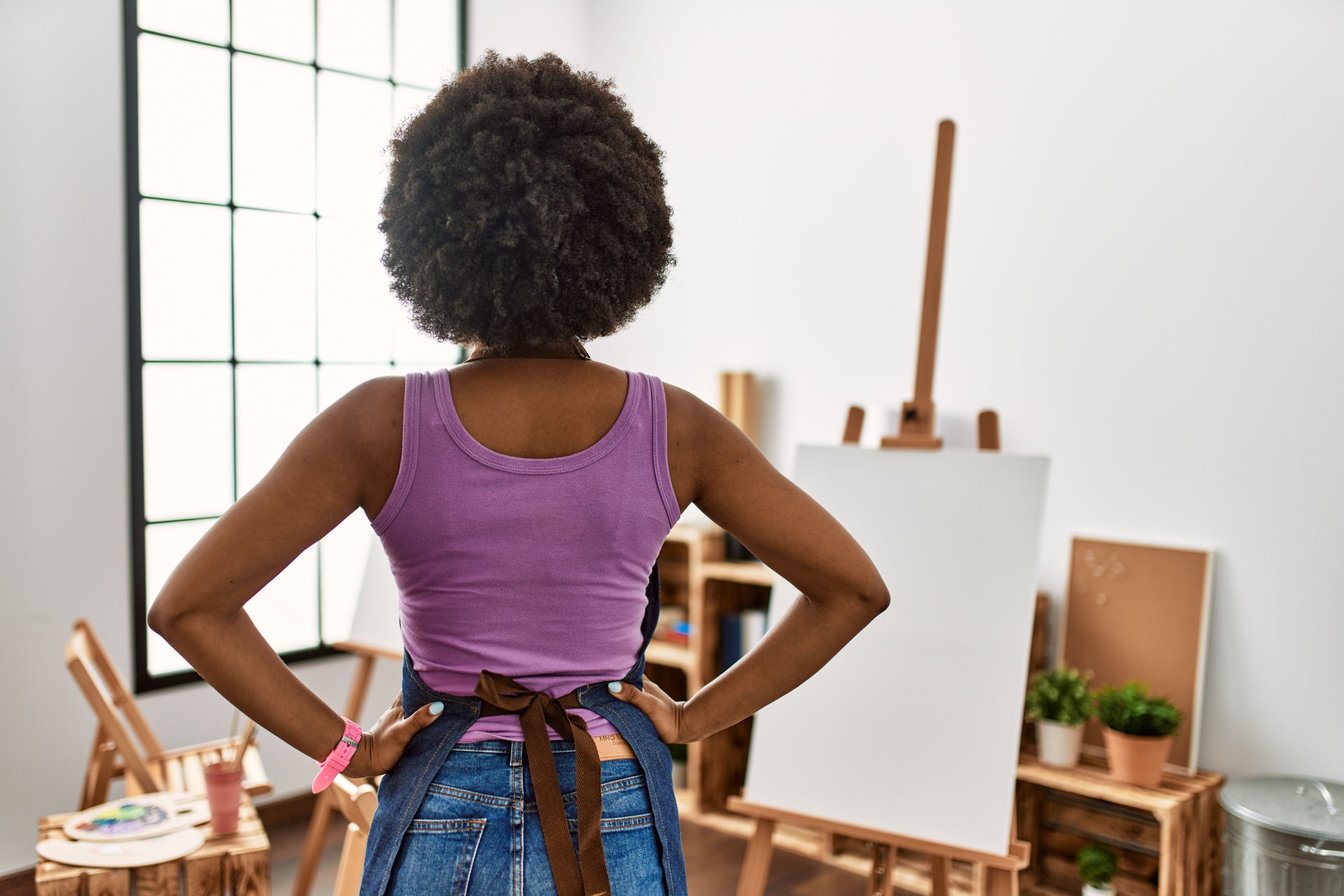 Young african american woman with afro hair at art studio standing backwards looking away with arms on body